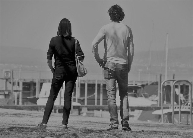 двоє людей, повернувшись спинами, дивляться на гавань, кораблі на задньому плані, чорно-біле фото